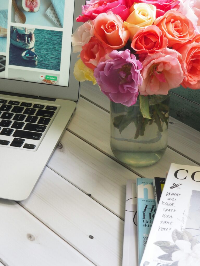 Bright and modern home office setup with a laptop, magazines, and a vibrant floral arrangement in a vase.